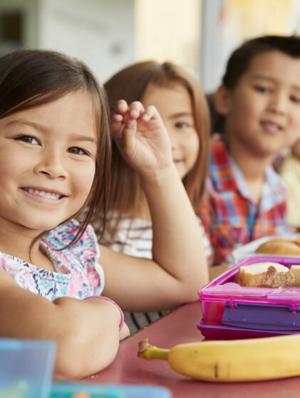Elementary school kids sitting a table with packed lunches