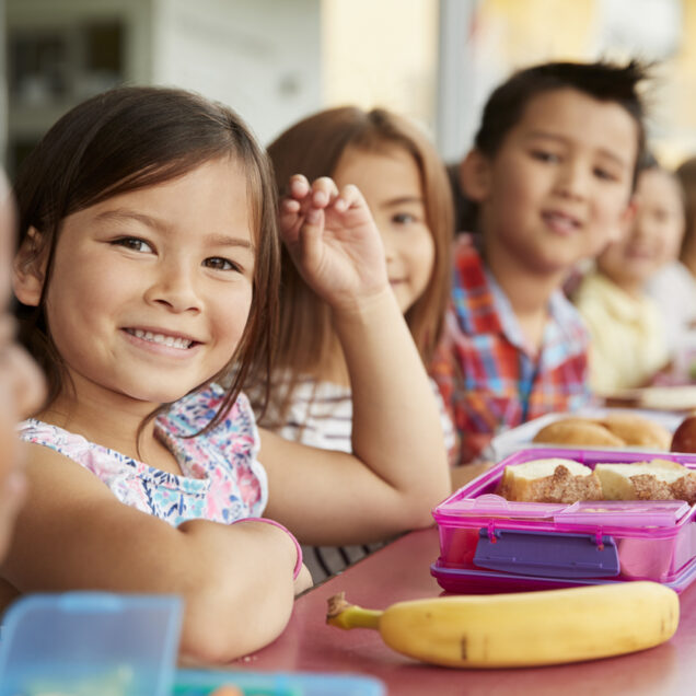 Elementary school kids sitting a table with packed lunches