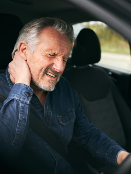 Senior man inside car after road traffic accident in pain suffering with whiplash injury