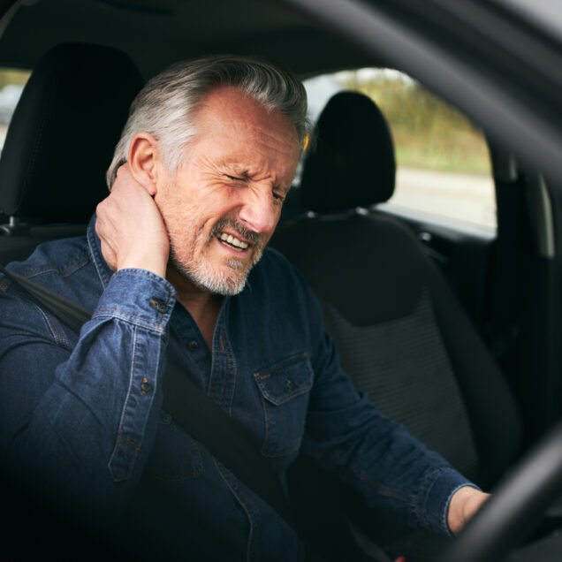 Senior man inside car after road traffic accident in pain suffering with whiplash injury