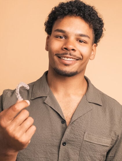 Happy young man showing invisible braces in beige studio