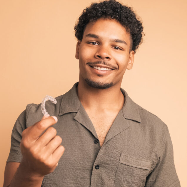 Happy young man showing invisible braces in beige studio
