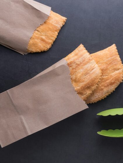 Aerial view of three Jamaican beef patties in brown paper bags with a tong on a black background