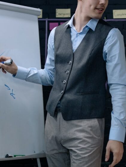 man in gret vest standing next to a whiteboard
