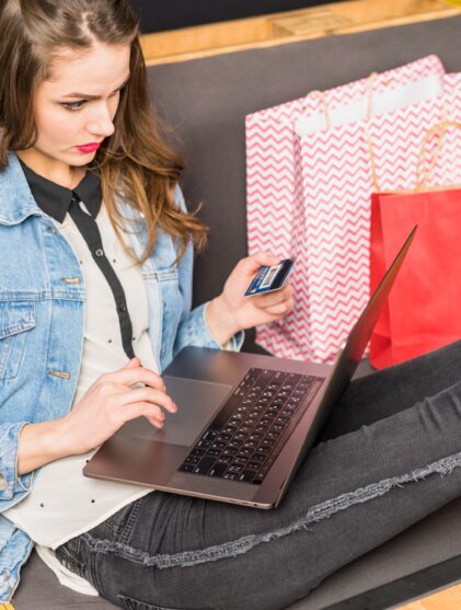 woman next to shopping bags while checking her credit card details and using her laptop