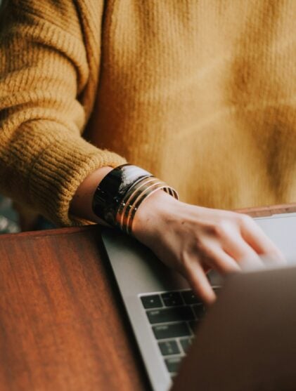 person in yellow brown sweater using a laptop