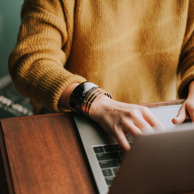 person in yellow brown sweater using a laptop