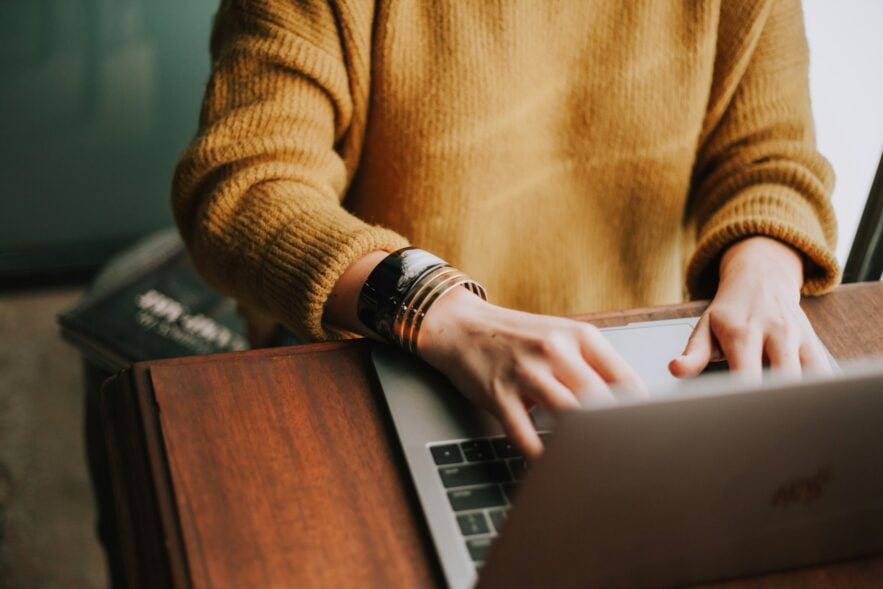 person in yellow brown sweater using a laptop